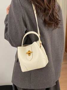 Chic cream white leather bucket bag with gold clasp shown on model in a stylish blazer