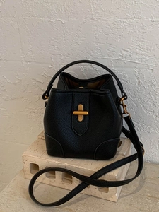 Elegant black pebble leather bucket bag with gold metal clasp on stone pedestal