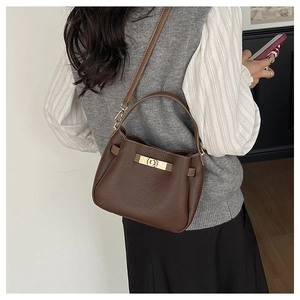 Détail d'un sac marron foncé en cuir grainé avec fermoir doré rotatif et bandoulière amovible