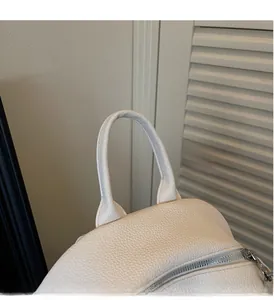 Macro detail of the thickened leather handle and silver metal zipper on a white backpack
