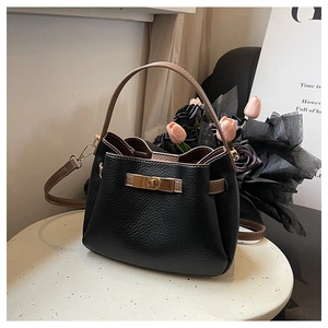 Gros plan du sac seau en cuir noir grainé avec détail de fermoir rotatif doré