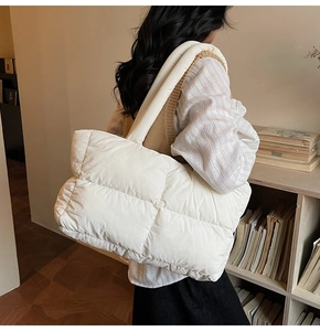 Side view of a large white quilted puffer tote bag carried by a model in a library