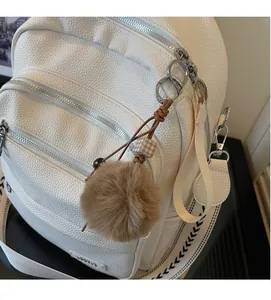 Detail of white lychee leather backpack showing silver zippers and plush ball charm