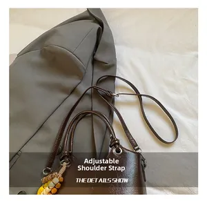 Detail der dunkelbraunen glänzenden Beuteltasche mit verstellbarem Riemen und Perlenanhänger
