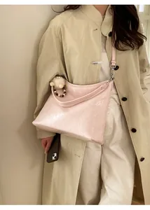 Detail of pink patent leather shoulder bag with plush charm and ruched texture on model