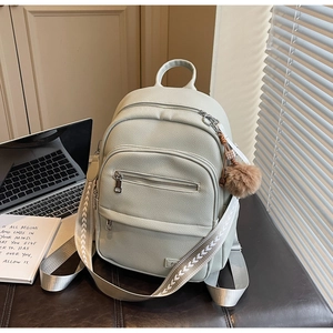 Detail of sage green faux leather backpack with woven strap and brown plush keychain