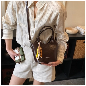 Detail of a shiny brown leather bucket bag with fashion beads and YIMING branding