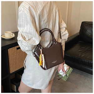 Detail view of dark coffee glossy leather tote with beaded charm and shoulder strap