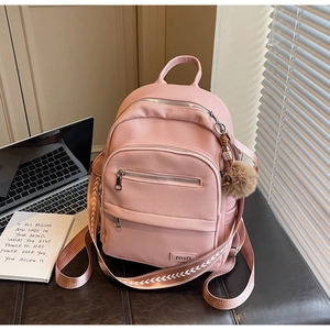 Detail view of pink pebbled leather backpack with woven strap and a cute pompom charm