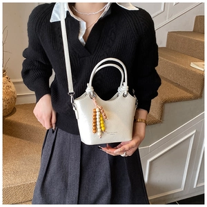 Detail of white bucket bag with beaded tassel charm and knotted handle on a model