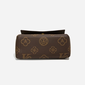 Detail der braunen Handtasche aus Leder mit Lychee-Narbung und gelbem Grafikmuster