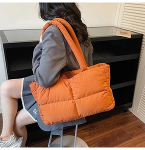 Detailed back view of a puffy orange quilted tote bag worn by a model in a minimalist setting