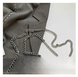 Close-up of thick silver metal chain strap on brown leather bag with gray blazer background