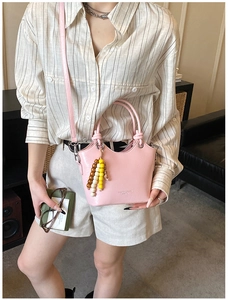 Detail of light pink patent leather bucket bag with unique knotted handle and beaded charm