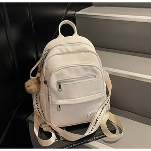 Close-up of white pebble grain leather backpack featuring a plush charm and canvas straps