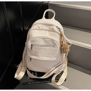 Detail of cream white faux leather backpack texture with silver zippers and pompom charm