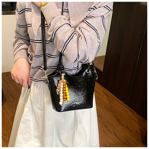 Detail of black glossy bucket bag with colorful beaded charm and slim leather strap