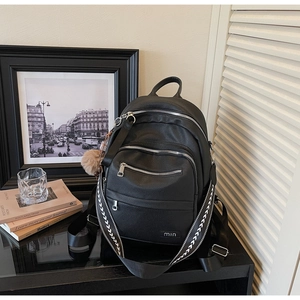 Detail of black pebbled leather backpack with silver zippers and plush ball charm accessory