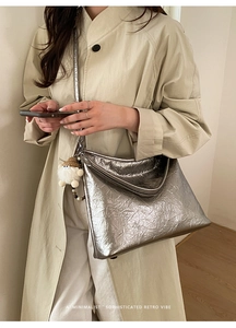 Detail of silver metallic wrinkled tote bag with cute doll charm on beige trench coat