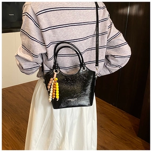 Detail of black glossy patent bucket bag with colorful wooden beads and fashion logo