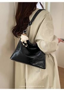 Detail of black glossy crinkled leather underarm bag with white plush doll charm