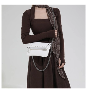 Detail of white leather crossbody bag featuring silver stud rivets and a sleek chain strap