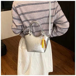 Detail of silver bucket bag with metallic texture, wood bead charm and handle