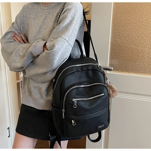 Side view of a black pebble leather backpack with silver zippers and a brown plush charm