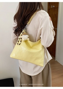 Detail of yellow wrinkled hobo bag with plush pendant and beaded strap on shoulder