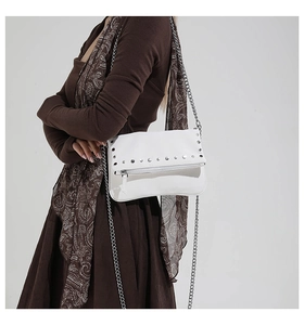Detailed view of white crossbody bag with silver metal rivets and chain strap on model