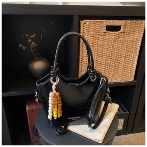 Detail of a black patent leather bucket bag with colorful bead tassel and wave trim