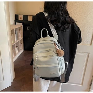 Detail of mint green lychee grain leather backpack with zip pockets and pompom charm