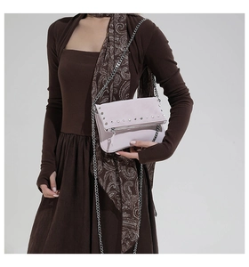 Detail of lavender crossbody bag with silver studs and metal chain strap on model