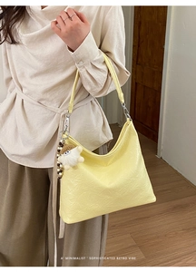 Pale yellow hobo bag with textured leather and a plush charm on a model's shoulder
