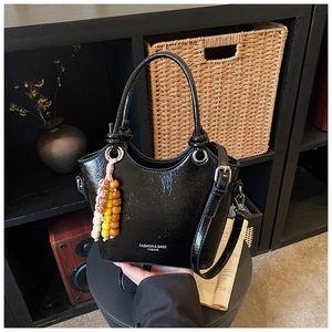 Detail of black glossy bucket bag featuring white lettering and colorful beaded charm