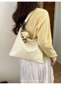 Chic cream underarm bag with glossy patent leather finish shown on model's shoulder
