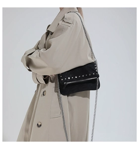 Model wearing black suede crossbody bag with silver studs and chain strap on beige trench coat