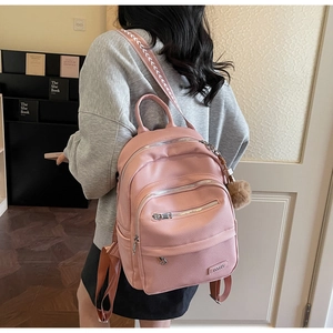 Pink faux leather backpack with plush ball charm and patterned straps shown on model