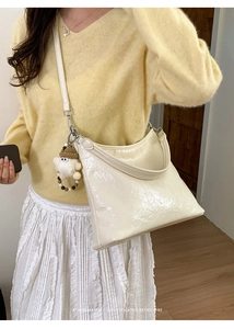 Close-up of cream hobo bag with glossy finish and cute plush charm on a model
