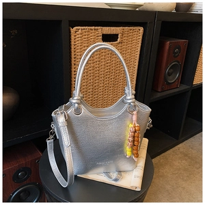 Detail of silver metallic bucket bag with textured finish and woven beaded keychain charm