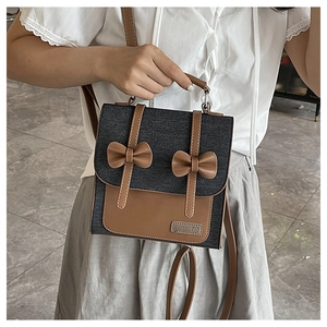 Detail of grey denim bag showing brown leather bows, branding label and shoulder strap