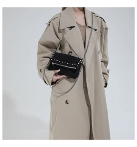 Detail of black suede crossbody bag with silver studs and chain strap on beige coat