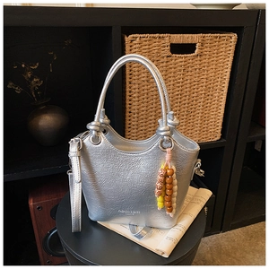 Detail of silver metallic tote bag featuring knotted handles and beaded charm accessory