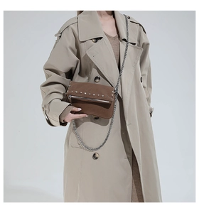 Brown suede crossbody bag with silver studs and chain styled on a beige trench coat