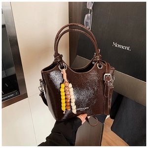 Close-up of dark brown patent leather bucket bag with beaded tassel and knotted handle
