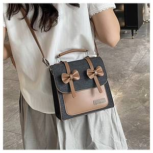 Detail of grey denim bag with leather trim and brown bow decorations worn by model