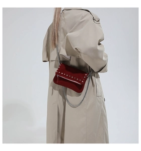 Detail of dark red suede crossbody bag with silver studs and chain on a beige coat