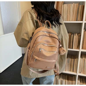 Close-up of light brown leather backpack with metal zipper detail and fur pompom accessory