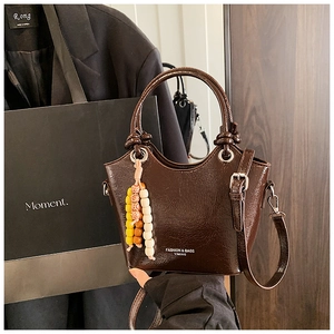 Detail of dark coffee patent leather bucket bag with colorful bead tassel and silver hardware