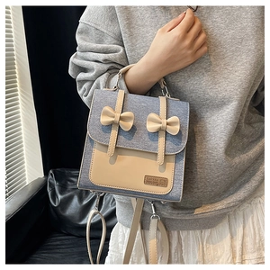 Détail du sac à dos en denim bleu avec nœuds beiges porté par un mannequin en intérieur